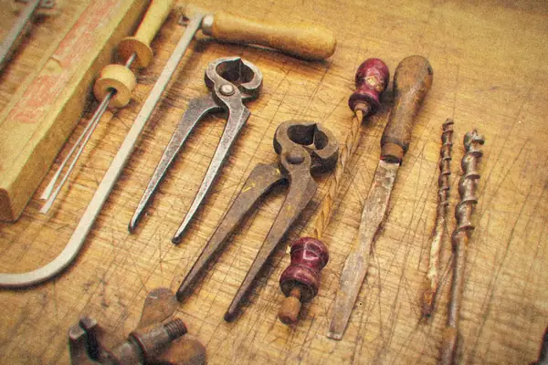 Old pincers, screwdrivers, a file and drill bits laid out on a scarred workbench.
