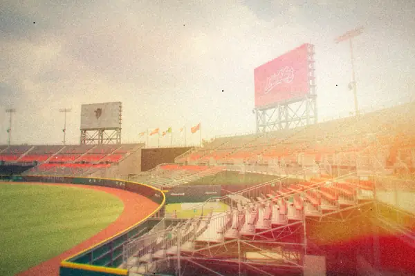 An empty baseball stadium with red seats and a scoreboard under a cloudy sky.