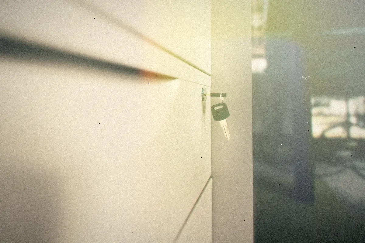 A small key left in the lock of a white metal office cabinet drawer.
