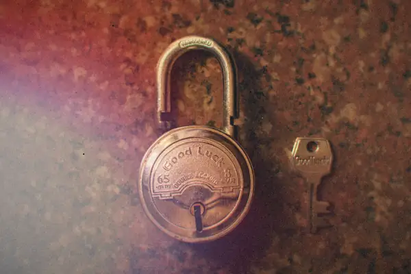 A round brass padlock and its key lying on a speckled stone surface.