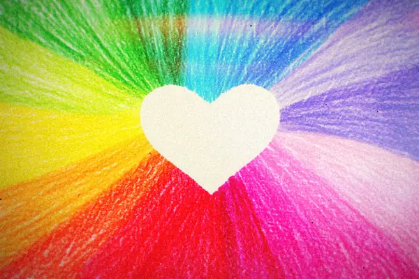 A white heart drawn in the middle of bright rainbow crayon strokes.