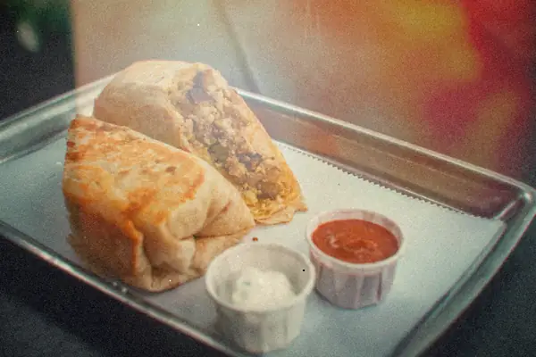 A breakfast burrito cut in half on a metal tray, with cups of salsa and sour cream.