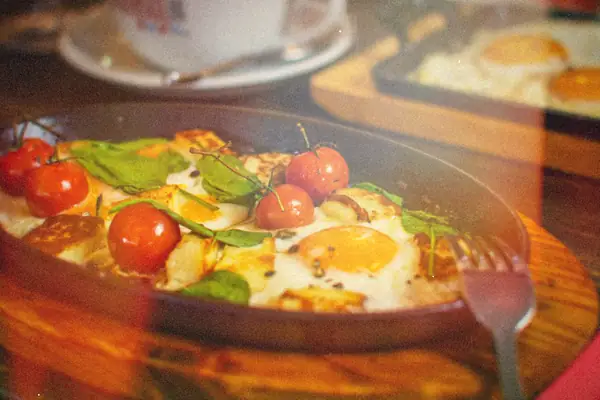 A cast-iron skillet of baked eggs with cherry tomatoes, spinach and seasoning on a wooden board.