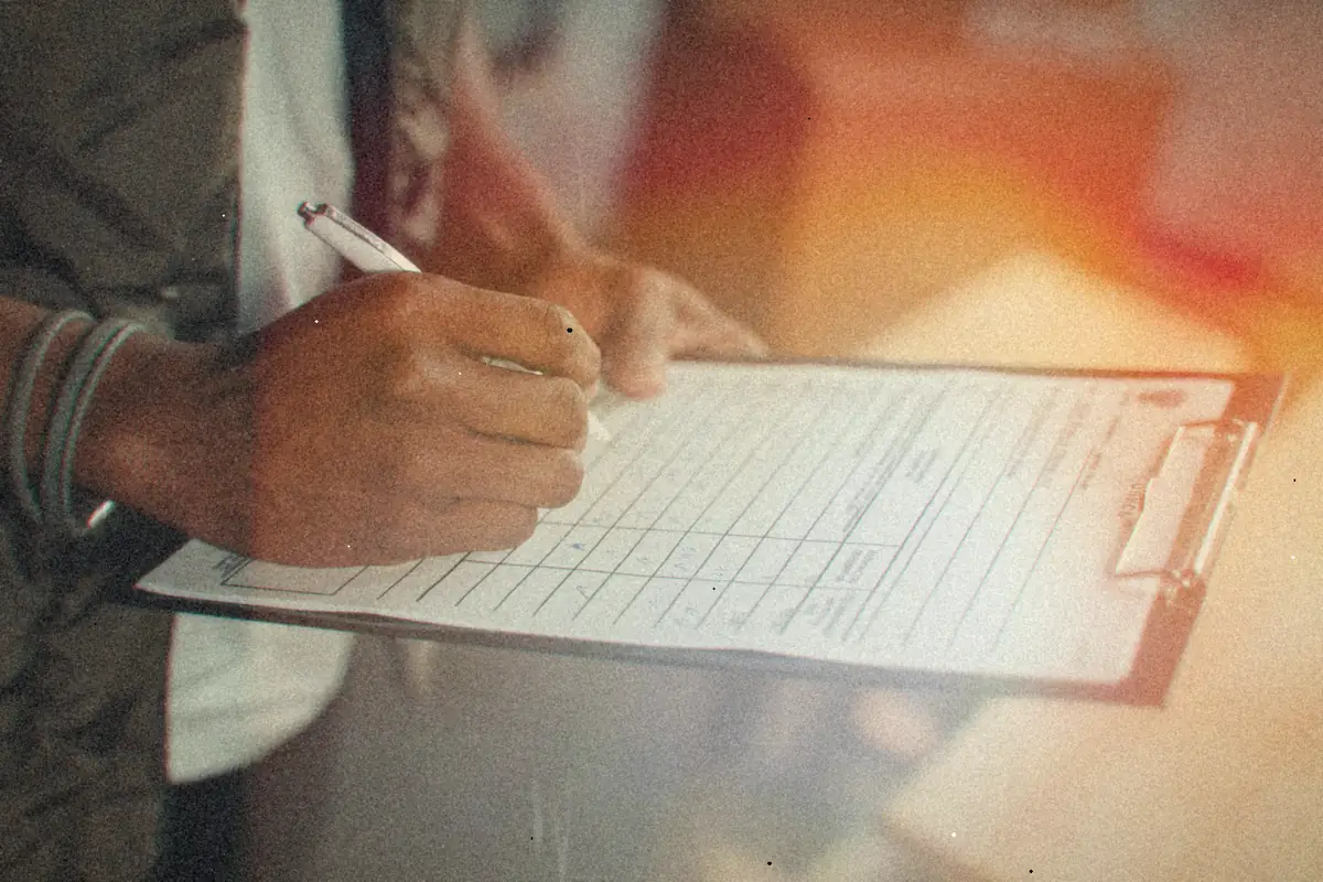 A hand filling in a form on a clipboard with a pen.