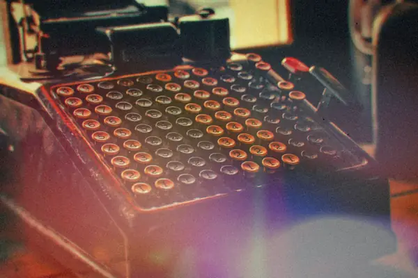 A vintage adding machine with rows of round number keys on a wooden desk.