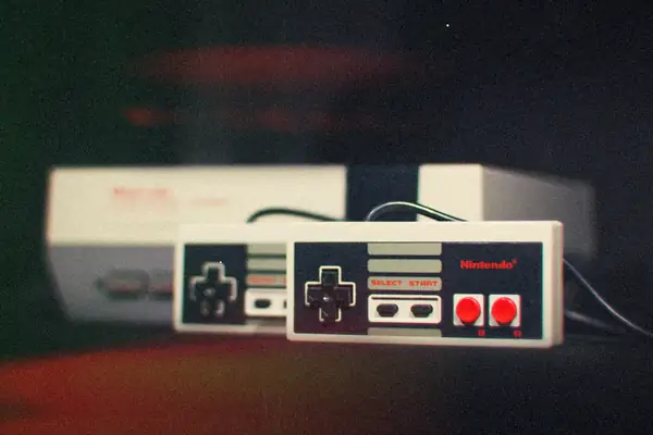 A grey NES-style console with two rectangular controllers in front of it against a black background.
