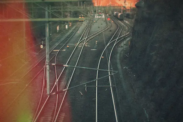 Many railway tracks curving together into one junction below overhead wires.