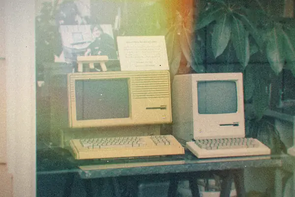 Early beige Apple computers with keyboards displayed in a shop window.