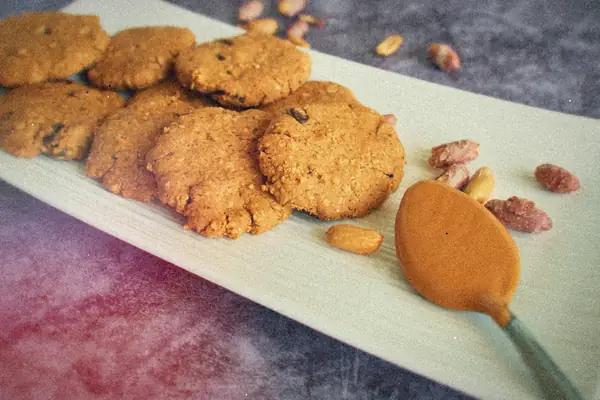 Peanut butter cookies on a white platter with peanuts and a spoonful of peanut butter.