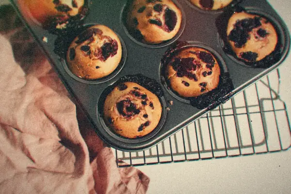 Jam-studded muffins in a dark muffin tin on a cooling rack.