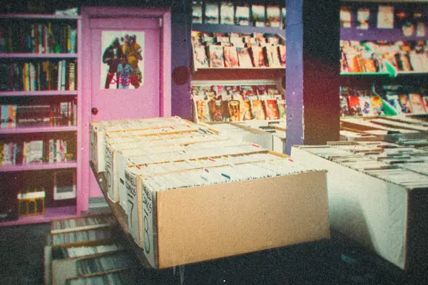 Long boxes of comic books on tables in front of shelves in a comic shop.
