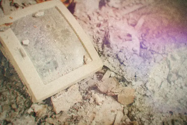 An old cracked computer monitor lying discarded in dusty rubble.