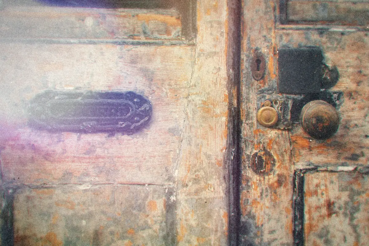 An old mail slot and door handle on a weathered wooden door.