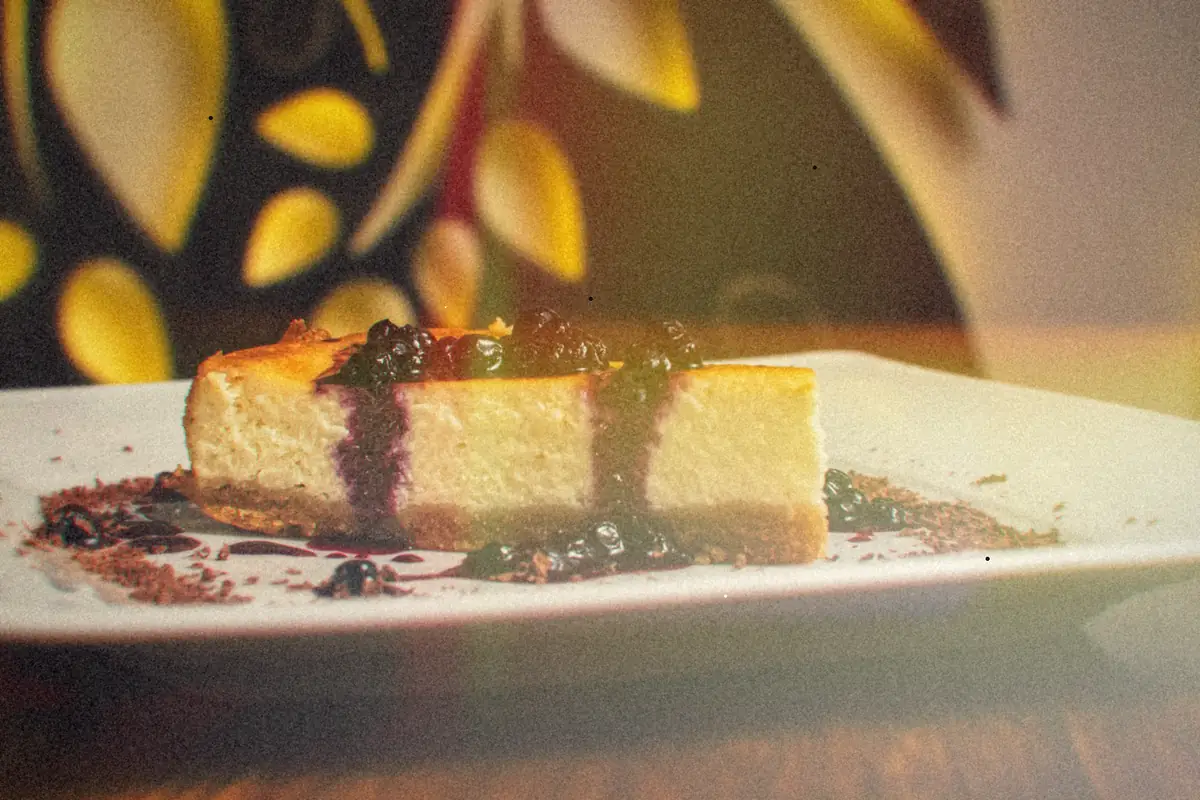 A slice of cheesecake topped with blueberries and blueberry sauce on a white plate.