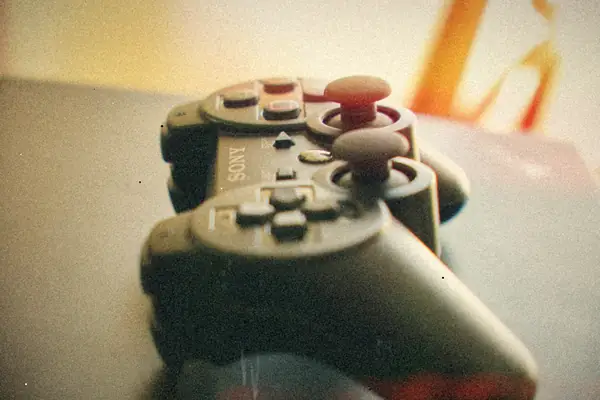 Two black PlayStation 3 controllers stacked on a dark surface, shot close with a soft background.