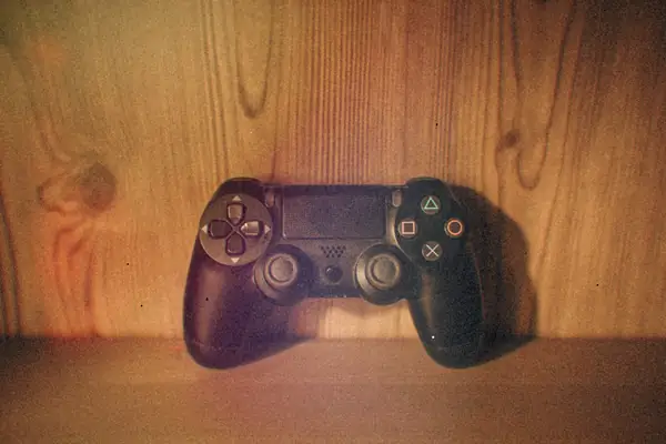 A black PlayStation 4 controller propped up on an empty wooden shelf.