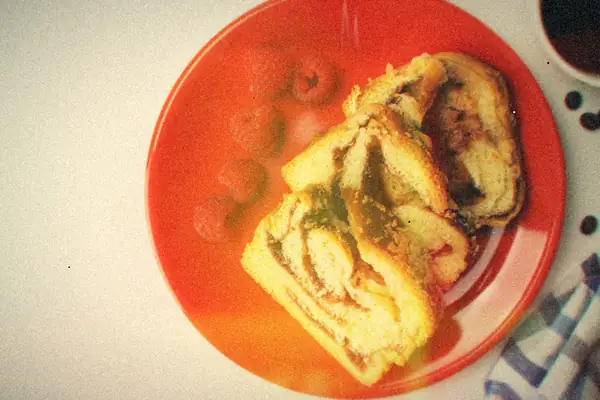 Slices of swirled coffee cake on a red plate with fresh raspberries and a cup of black coffee.