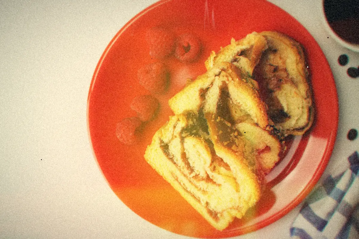 Slices of swirled coffee cake on a red plate with fresh raspberries and a cup of black coffee.