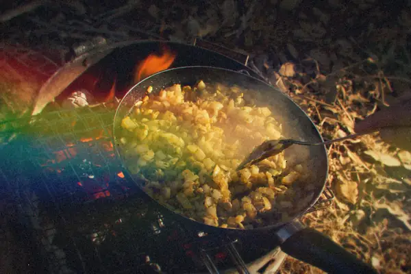 Diced potatoes crisping in a skillet over a campfire grill.
