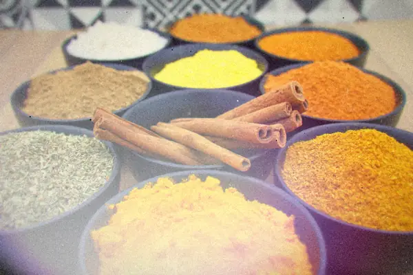 Black bowls of ground spices, dried herbs, salt and cinnamon sticks arranged on a wooden table.