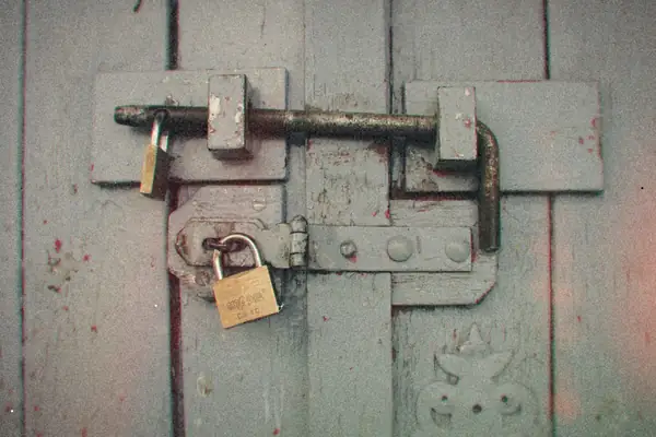 A weathered wooden door secured with a sliding bolt and brass padlocks.