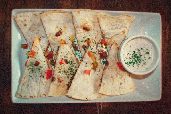 Quesadilla wedges with diced peppers and herbs on a rectangular platter with a creamy dip.