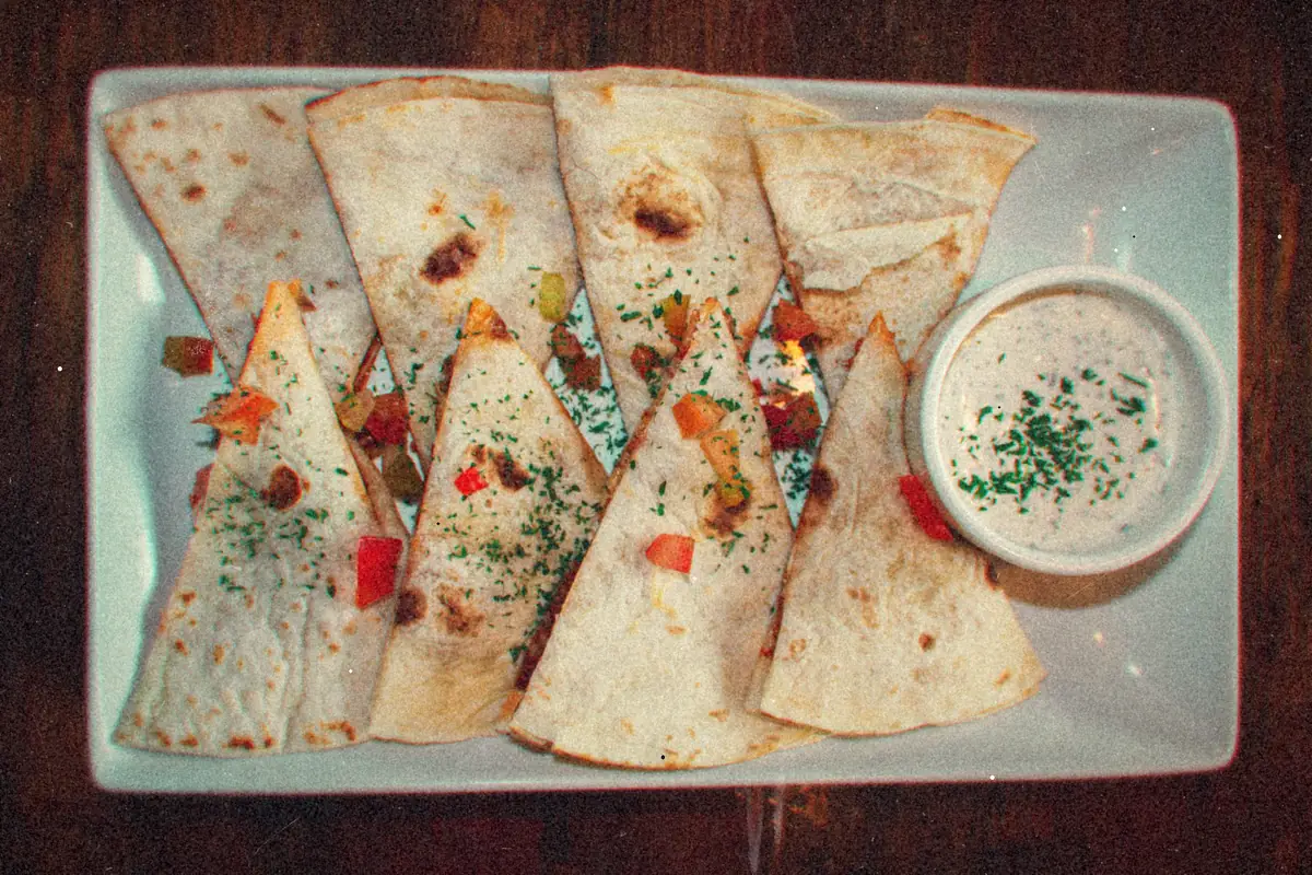 Quesadilla wedges with diced peppers and herbs on a rectangular platter with a creamy dip.