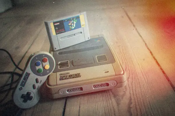 A grey Super Nintendo with a cartridge in the slot and a controller beside it on worn wooden floorboards.