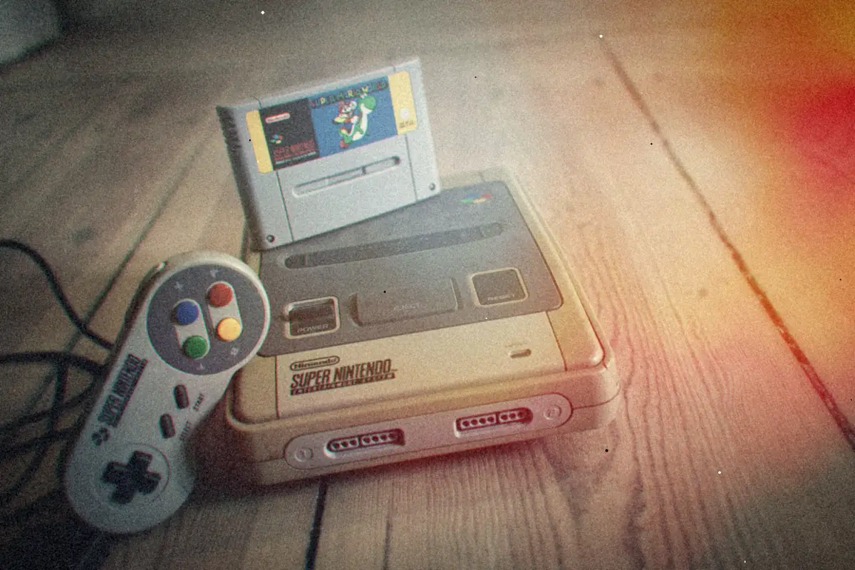 A grey Super Nintendo with a cartridge in the slot and a controller beside it on worn wooden floorboards.