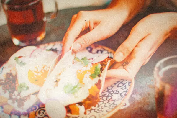 Hands fold warm tortillas topped with fried eggs, crumbled chorizo and herbs.