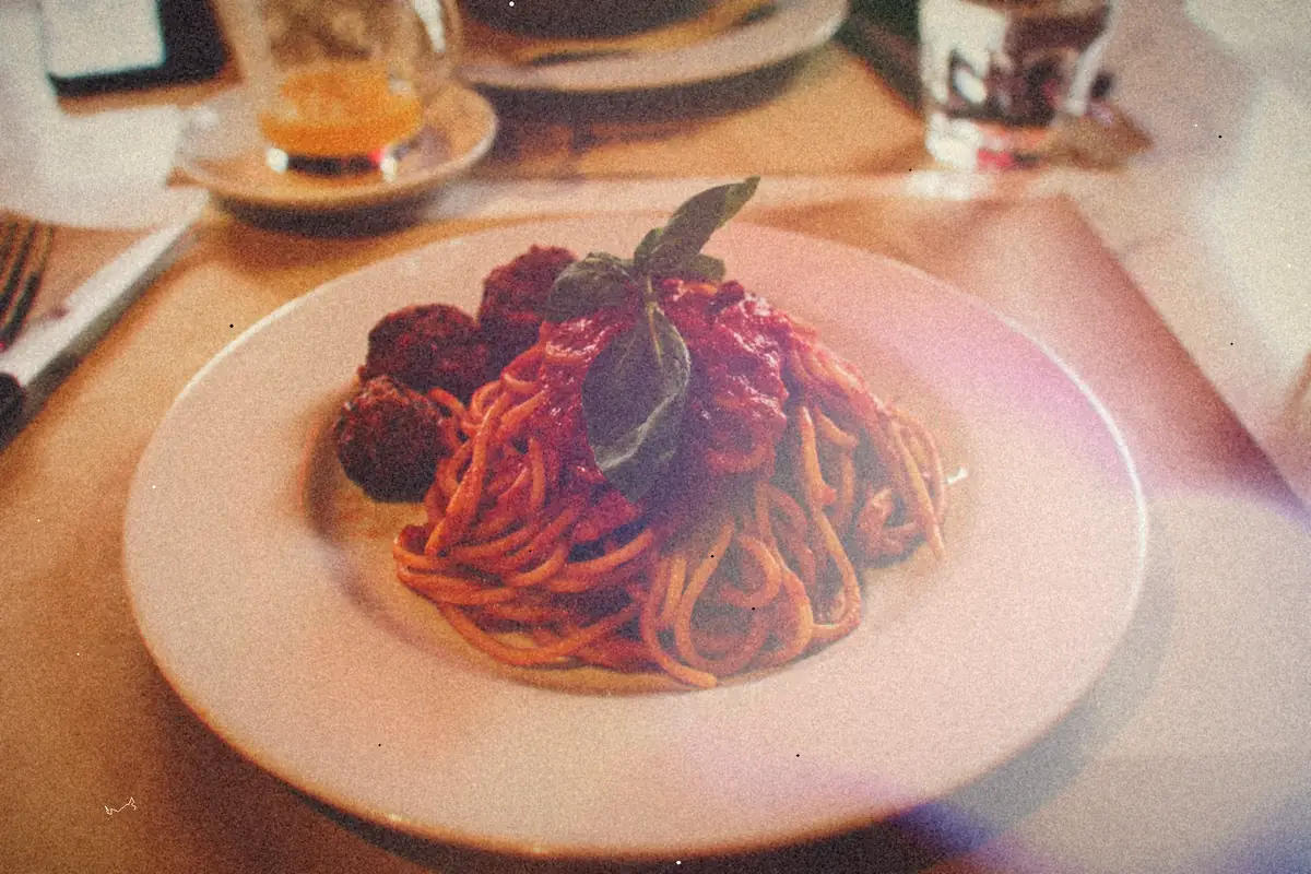 A plate of spaghetti in tomato sauce with meatballs and a sprig of fresh basil.