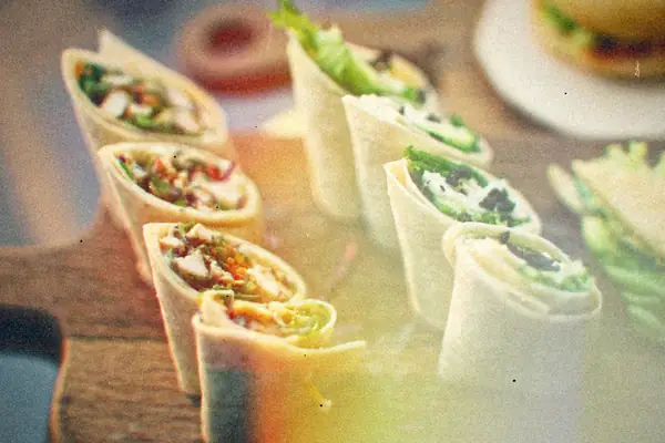 Cut tortilla wrap pieces filled with leafy greens and white cheese, standing on a wooden board.