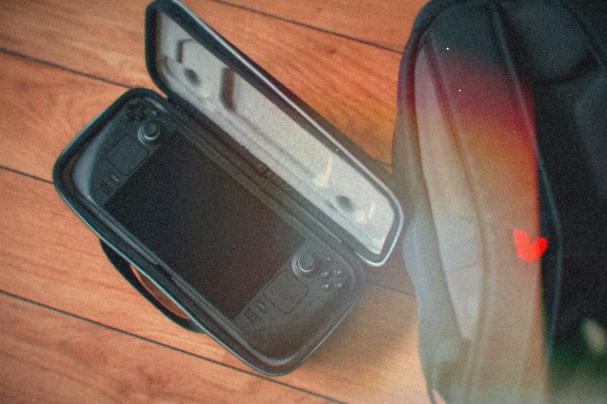A Steam Deck resting in its open carrying case on a wooden floor next to a black backpack.
