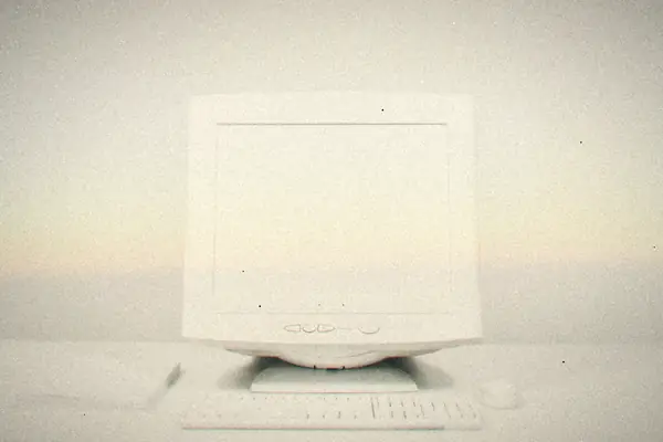 A late-'90s white CRT monitor with a matching keyboard and mouse on a plain white desk.