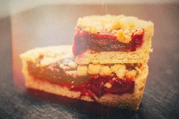 Two stacked crumble bars with a red berry filling and a buttery crumb topping on a dark slate.