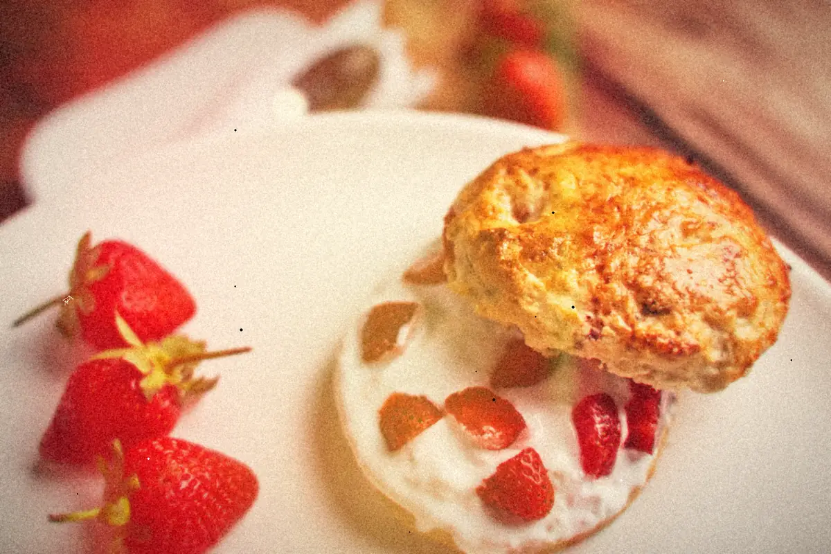 A split biscuit strawberry shortcake with cream and chopped strawberries on a white plate.