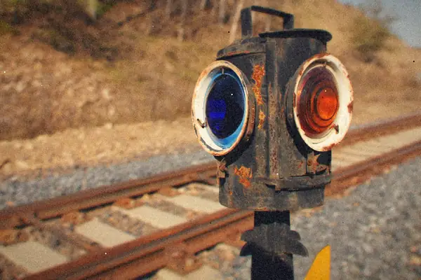 A rusty old railroad signal lamp with blue and amber lenses beside the tracks.