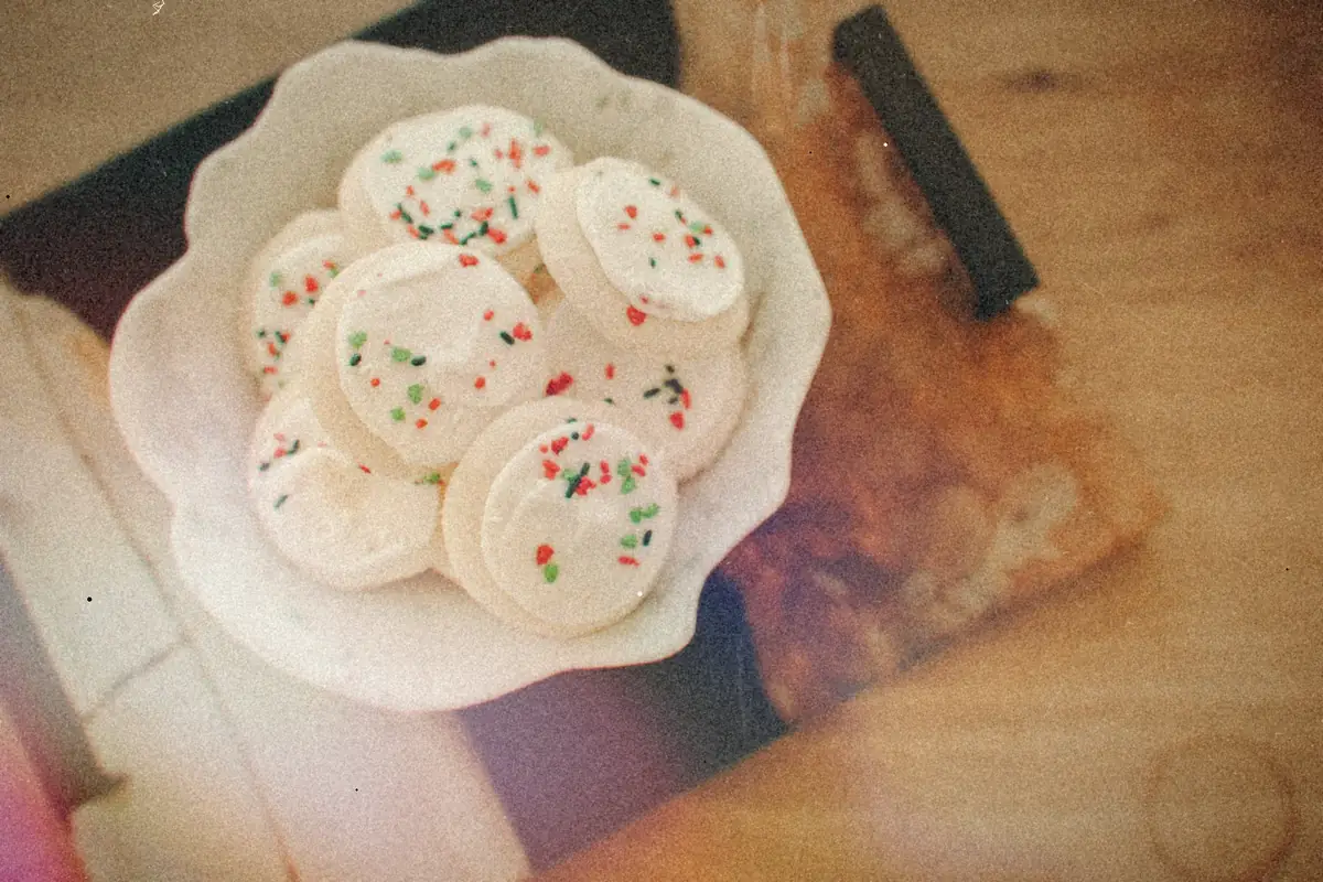 A white bowl of frosted sugar cookies with red and green sprinkles on a wooden tray.