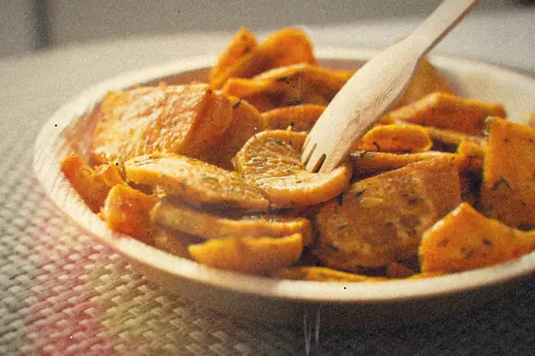 A bowl of crispy roasted sweet potato pieces with herbs and a wooden fork.