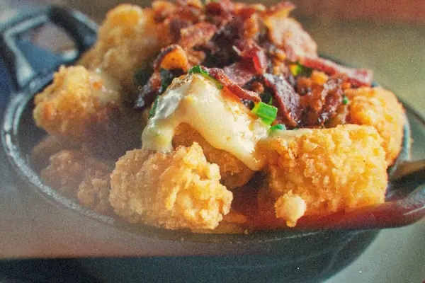Crispy tater tots topped with melted cheese and bacon in a cast iron skillet.