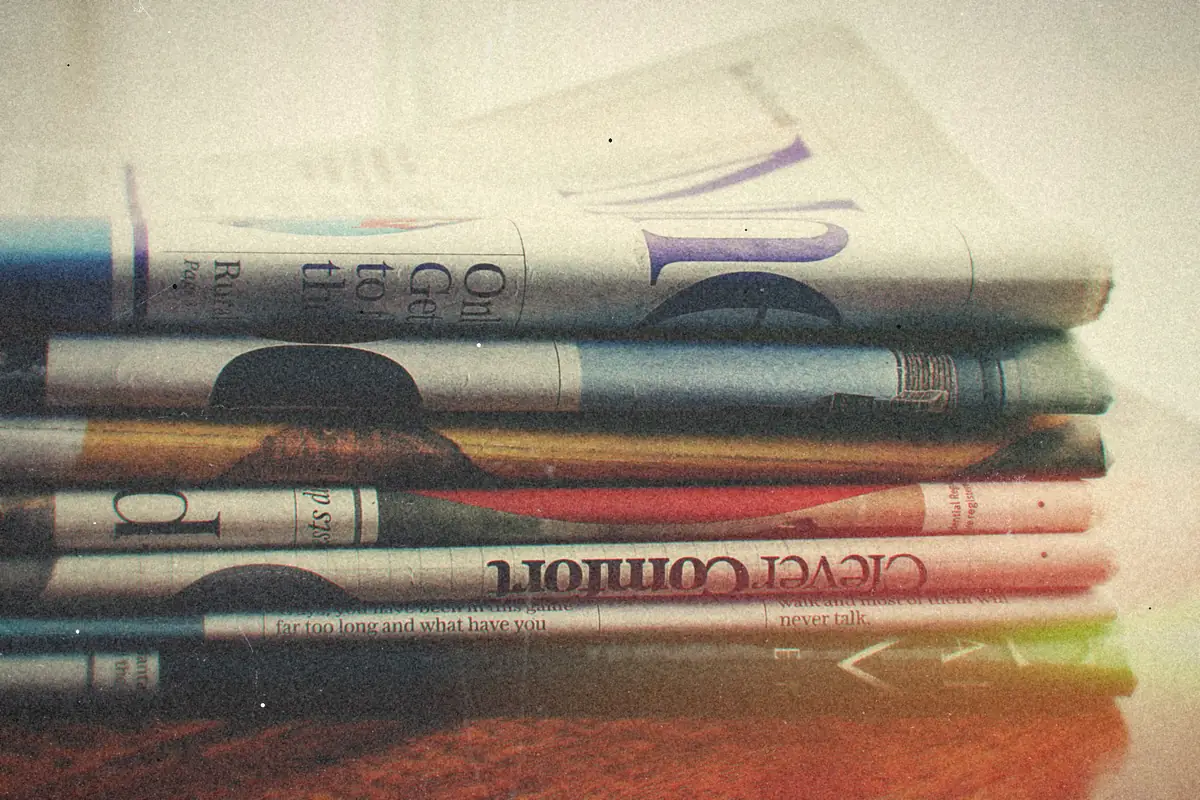 A stack of folded newspapers resting on a wooden table.