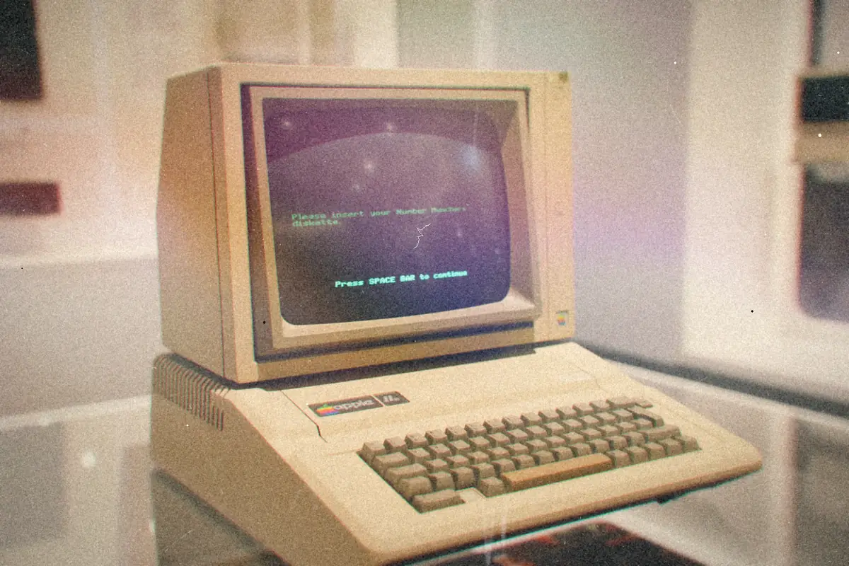 A vintage Apple II computer with green text glowing on its monitor.