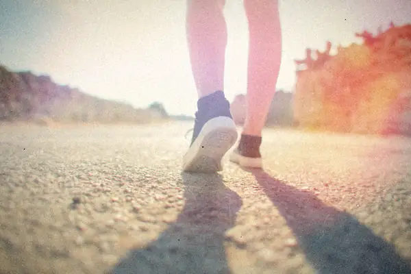 Low view of sneakers walking down a sunny country road.