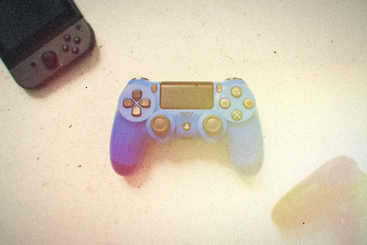 A pastel blue game controller on a white desk next to a handheld console.