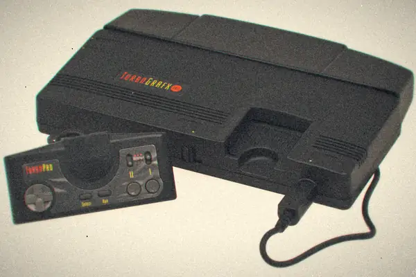 A black TurboGrafx-16 console with its TurboPad controller plugged in, on a plain white background.