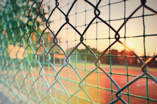 A chain link fence at a sports field with the evening sun low behind it.