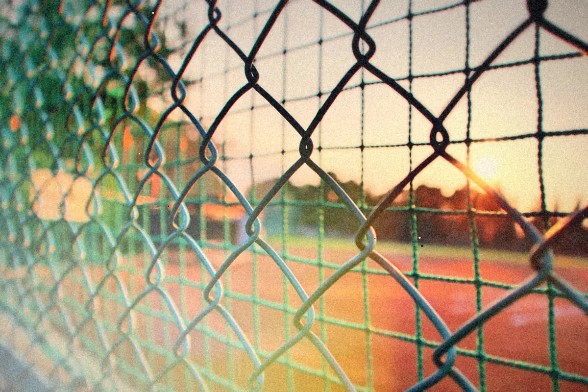 A chain link fence at a sports field with the evening sun low behind it.