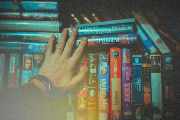 A hand reaching for a tape on a shelf packed with old VHS movie cases.