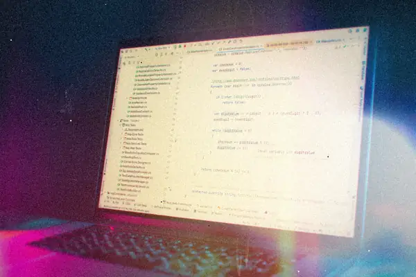 A laptop screen full of code in a light editor theme, lit blue and pink from the side.